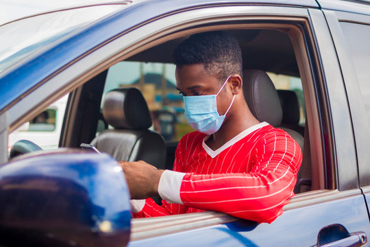 Young Handsome African Taxi Driver Wearing Face Mask Preventing, Prevent, Prevented Himself From The Outbreak In The Society And Operating His Mobile Phone