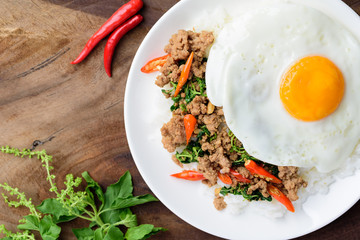 Thai food, stir-fried holy basil with minced pork and fried egg (Pad Kaprao Moo Kai Dao) on wooden background, Top view