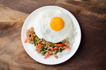 Thai food, stir-fried holy basil with minced pork and fried egg (Pad Kaprao Moo Kai Dao) on wooden background, Top view