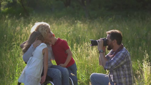 Father takes photographs of a family with his mother in a wheelchair enlarging outdoors in the park or garden. Loving Family Concept. Prores 422. 