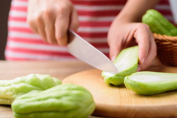 Woman cutting chayote squash or mirlition squash on  wooden board, Organic vegetable, Edible plant fruit