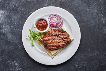Grilled meat steak with onions, sauce and microgreen, on pita bread, on a white plate, against a dark background. space for text. top view