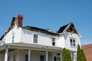 The burned house has roof damage. The windows are broken on the fire damaged house.
