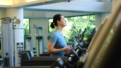 Attractive young sports woman is working out in gym doing cardio training running on treadmill in sport club