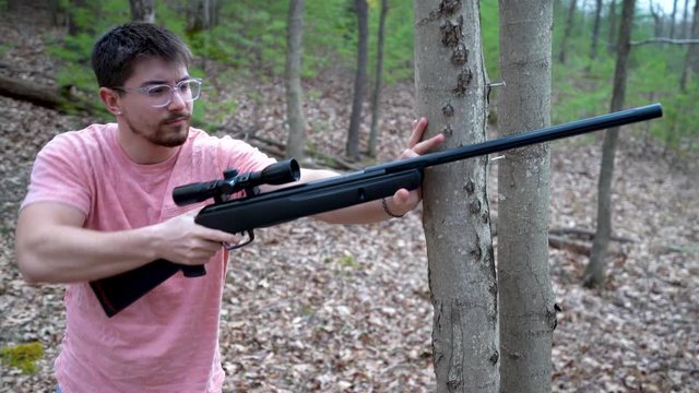 Young hipster man aims and fires a pellet rifle in a forest.