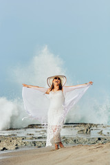 Happy free-spirited latina woman with open arms wearing white clothes and a hat on the beach