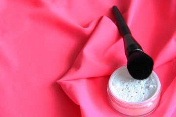 makeup brush and powder, women's face cosmetics, transparent powder and powder brush on a pink background close-up