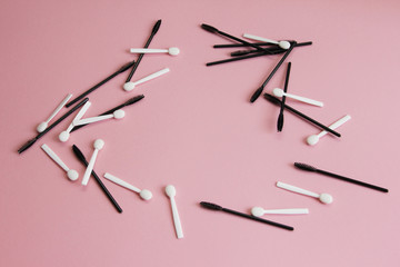 mascara brushes and shadow applicators are scattered carelessly on a pink background