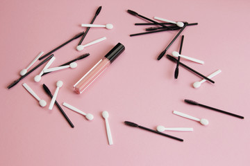 mascara brushes and shadow applicators and lipstick on a pink background are scattered carelessly