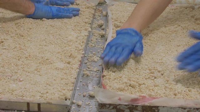 Close up of factory cake baking. Two workers wearing gloves prepare spread cake mixture on trays ready for the oven
