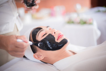 Obraz na płótnie Canvas Spa and beauty room, black face mask of mud and algae, an Asian woman lying on the bed, waiting for a mask expert on a beautiful face.