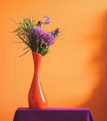 A bunch of purple violet spring flowers in an orange vase on warm yellow background. A colorful...