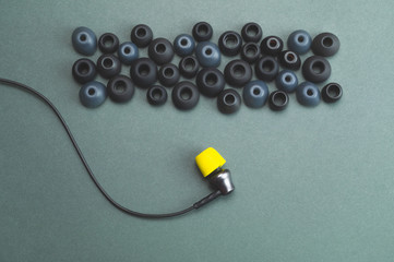 Individuality concept. earphone with yellow ear cushion opposite a row of gray embouchures. in-ear headphones. audio equipment