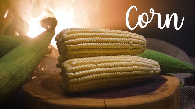 Three corn on a wooden board. Beside it appears written in English: Corn