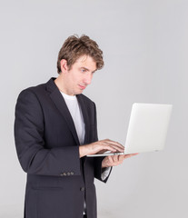 Portrait of handsome young businessman standing holding using laptop computer and checking email or confused more data, isolated on grey background.