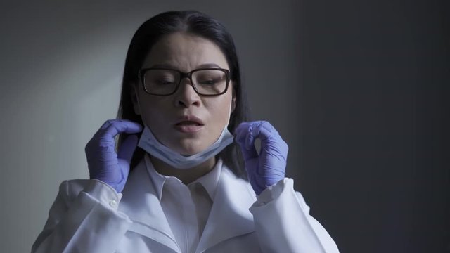 Exhausted microbiologist asian woman at the workplace takes off her face mask and goggles and touches her face with disposable gloves. Fatigue leads to indiscretion. Prores 422. 