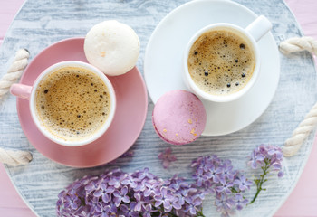 Close up pink and white cup with coffee and macaroon on wooden table. Nice summer background with  lilac flowers. Spring card template. Good, cozy morning concept. Spring, summer season. Copy space