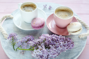 Close up pink and white cup with coffee and macaroon on wooden table. Nice summer background with  lilac flowers. Spring card template. Good, cozy morning concept. Spring, summer season. Copy space