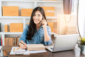 beautiful Asian businesswoman smiling using writing on parcel packaging, using computer laptop ecommerce online store selling delivering products, working at home office during quarantines isolation