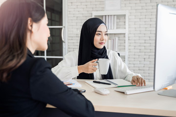 Obraz na płótnie Canvas multiethnic asian female muslim working in office as team having cup coffee using computer to strategize and planning, concept of diversity of different culture race type of people co-working together