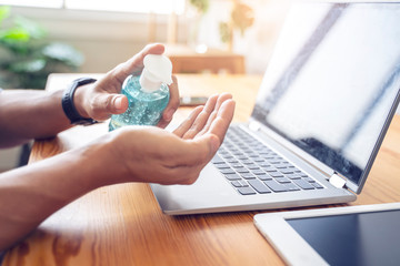 Asian businessman work from home self isolation in quarantine, stay safe with gel sanitizer cleaning hands and wearing facemask from coronavirus covid-19 infection, office room using computer laptop