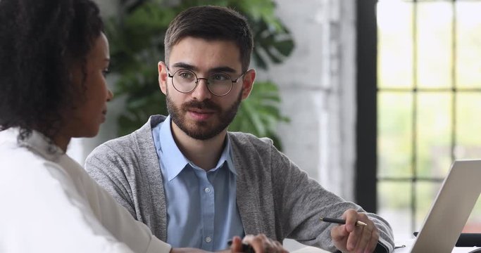 Head shot young professional financial consultant talking to mixed race female client, discussing business issues at meeting. Two diverse colleagues enjoying pleasant conversation ay workplace.