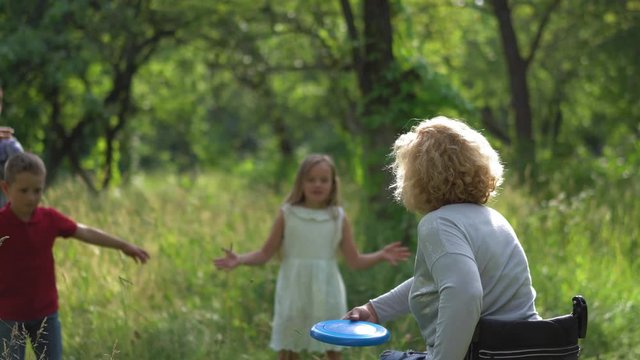 Mom in a wheelchair plays with herself on the line throwing Frisbee to children and dad is behind them a safety. Family concept. Prores 422. 