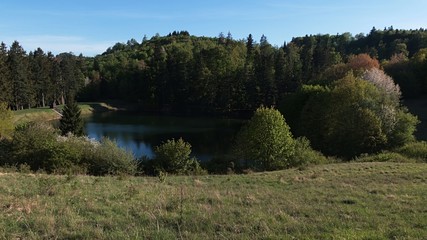 Fototapeta na wymiar Mountain landscape with artificial mining lake Bakomi in Stiavnica mountains during spring season. Broadleaf trees visible around the lake, coniferous forest in background. Afternoon sunshine. 