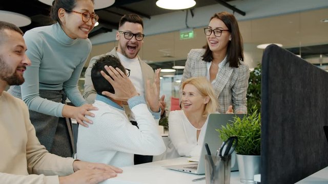 Multi-ethnic team women and men are talking clapping hands doing high-five celebrating achievement in open space office. People and work concept.