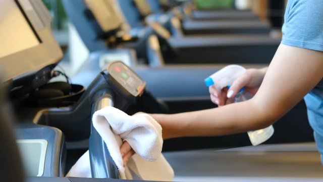Gym cleaning and disinfection. Infection prevention and control of epidemic. Staff using wipe and alcohol sanitizer spray to clean treadmill in gym. Anti Covid-19 precautions