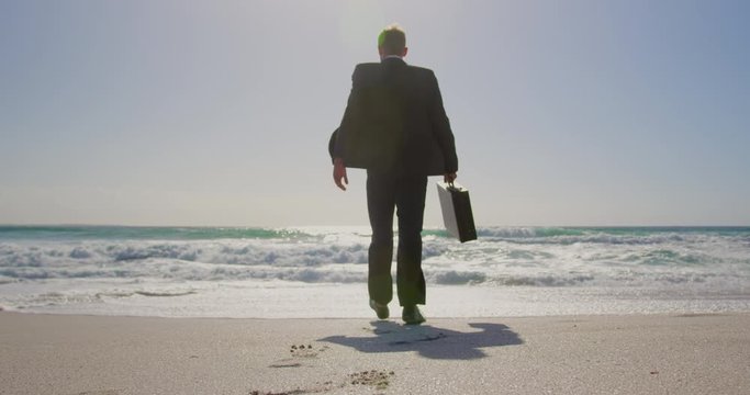 Businessman walking towards sea on beach in the sunshine
