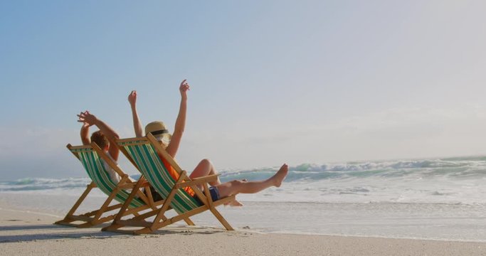 Couple with arms up relaxing on sun lounger at beach in the sunshine