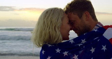 Couple wrapped in American flag at beach during sunset - Powered by Adobe