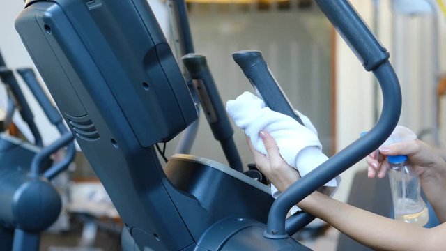 Gym cleaning and disinfection. Infection prevention and control of epidemic. Staff using wipe and alcohol sanitizer spray to clean elliptical trainer in gym. Anti Covid-19 precautions