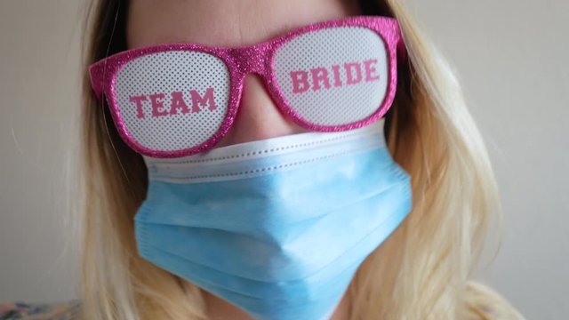 Even a pandemic wont stop team bride. Woman wears a face mask and pink glitter sunglasses to celebrate a bachelorette party. Shot signifies wedding showers and parties cancelled due to Covid-19. 