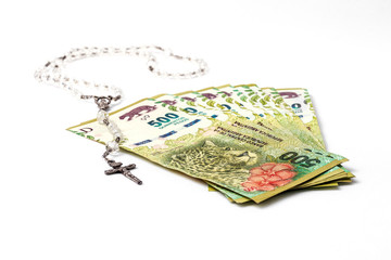 Fan of 500 Argentine pesos banknotes next to Catholic rosary isolated on white background 