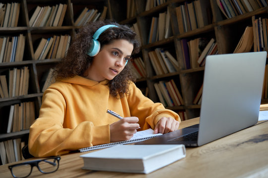 Hispanic Teen Girl, Latin Young Woman School College Student Wear Headphones Learn Watching Online Webinar Webcast Class Looking At Laptop Elearning Making Notes Or Video Calling Remote Teacher.