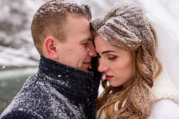 Groom snuggles up to his bride. Close-up. The couple is covered in snow. Winter wedding.