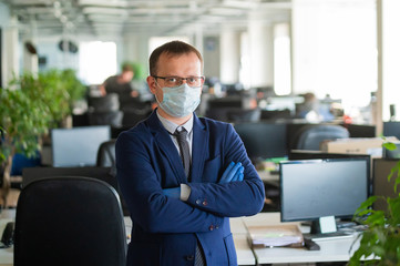 Businessman in medical mask and gloves works in an open space office. Male middle manager in a suit follows safety precautions during a coronavirus epidemic. Caring for the health of employees.