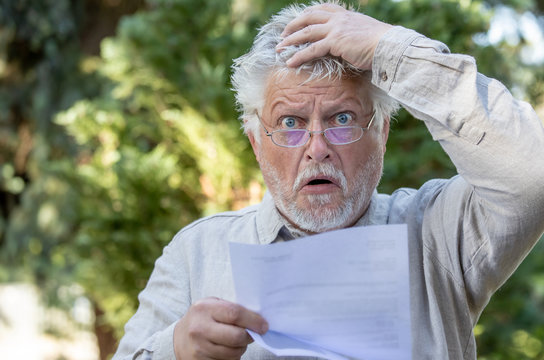 An older man reads a letter and is horrified. He wears glasses.