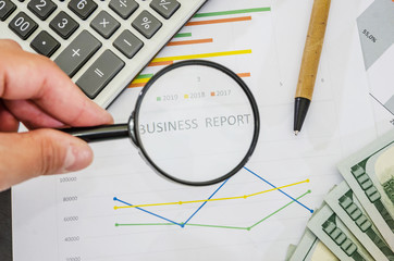 Consider the inscription “Business report” on a graph in a magnifying glass. View from above. Business concept. Revenue analysis and business development strategy.