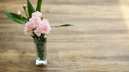 Light pink flowers in vase on wood background