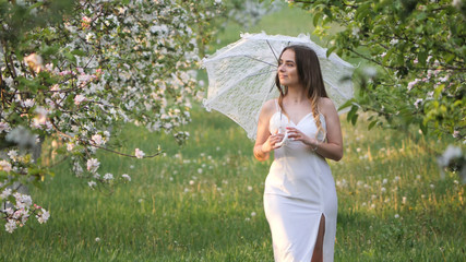 girl with a white umbrella in blooming apple trees in the garden
