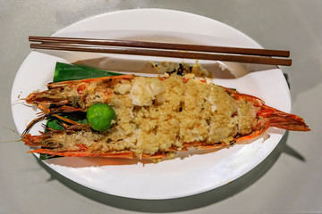 Large prawn or shrimp grilled with roasted garlic and lime on a plate with chopsticks at a hawker stall in Singapore