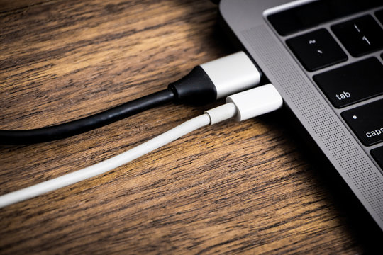 Detail of two usb-c connectors connected to a laptop on wooden table