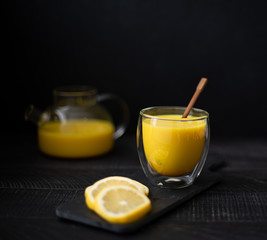 hot milk with turmeric and cinnamon in a glass bowl on a black background