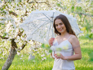 girl with a white umbrella in blooming apple trees in the garden