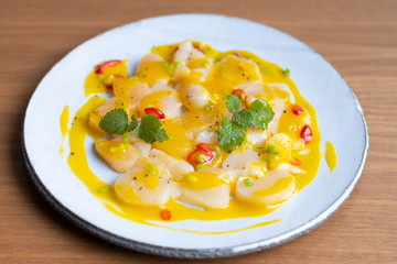 scallop with mango sauce and chili pepper on a white ceramic plate.