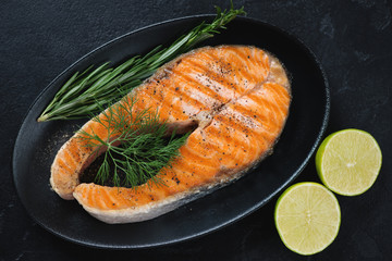 Roasted salmon steak with fresh dill, rosemary and lime served on a black plate, elevated view, horizontal shot