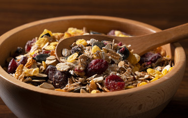 Granola and a wooden spoon in a vessel set against a wooden background
